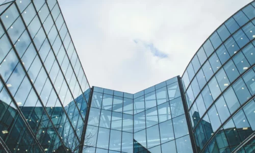 Modernos edificios de oficinas de cristal con ventanas reflectantes, vistos desde abajo contra un cielo nublado.