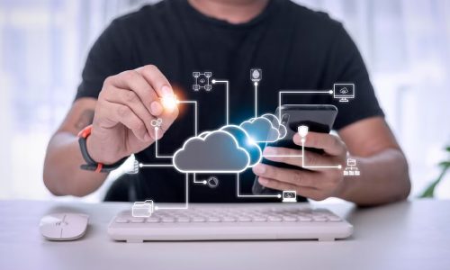 img-mesa-de-servicios Una persona opera un teléfono inteligente con una mano, mientras usa la otra para interactuar con íconos digitales conectados a un gráfico de nube, mientras está sentada en un escritorio con un teclado.