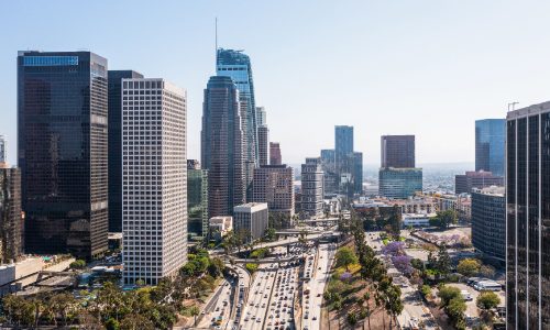 Vista aérea de un paisaje urbano con edificios altos y una autopista muy transitada que atraviesa el centro en un día claro.