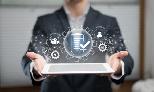 img-waf Persona que sostiene una tableta con un holograma que muestra íconos comerciales, incluida una lista de verificación, engranajes y símbolos de usuario, que representan la gestión de tareas digitales.